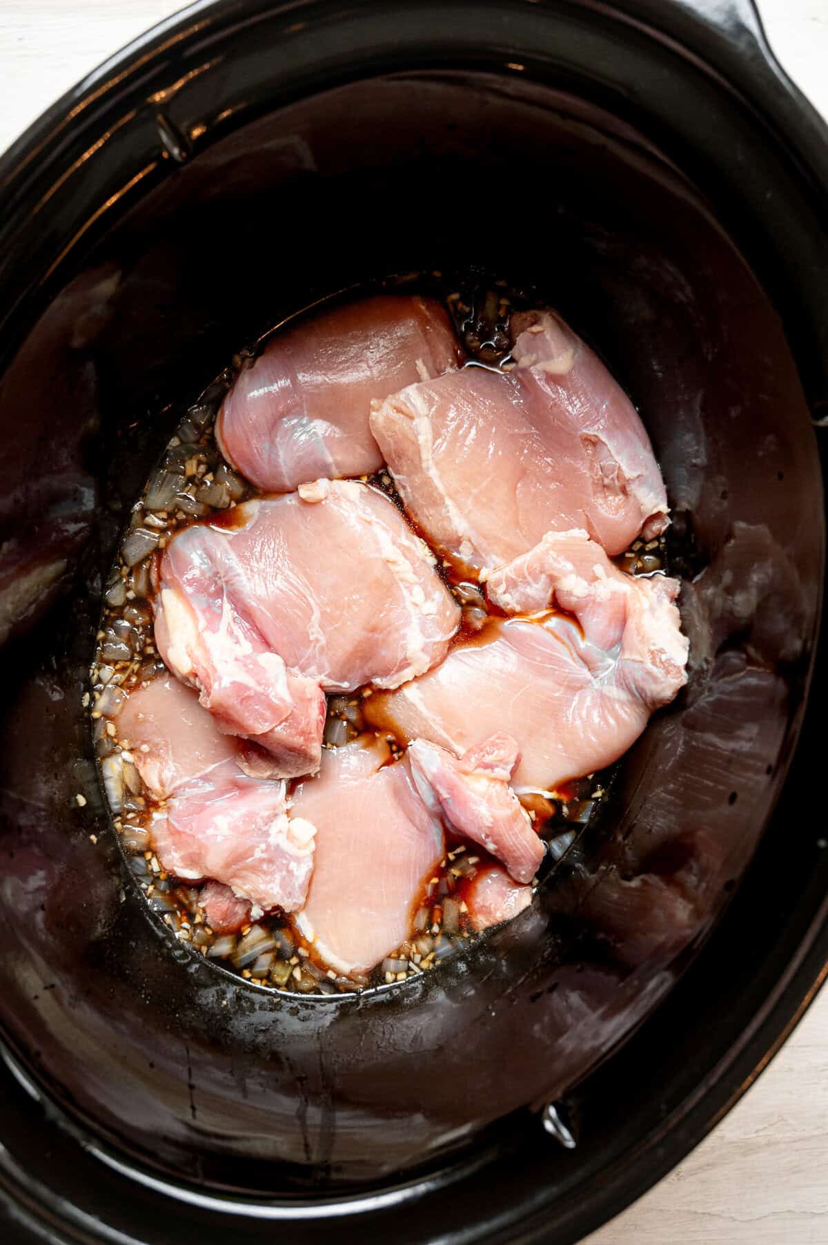 Raw boneless skinless chicken thighs in teriyaki sauce ingredients in a slow cooker.