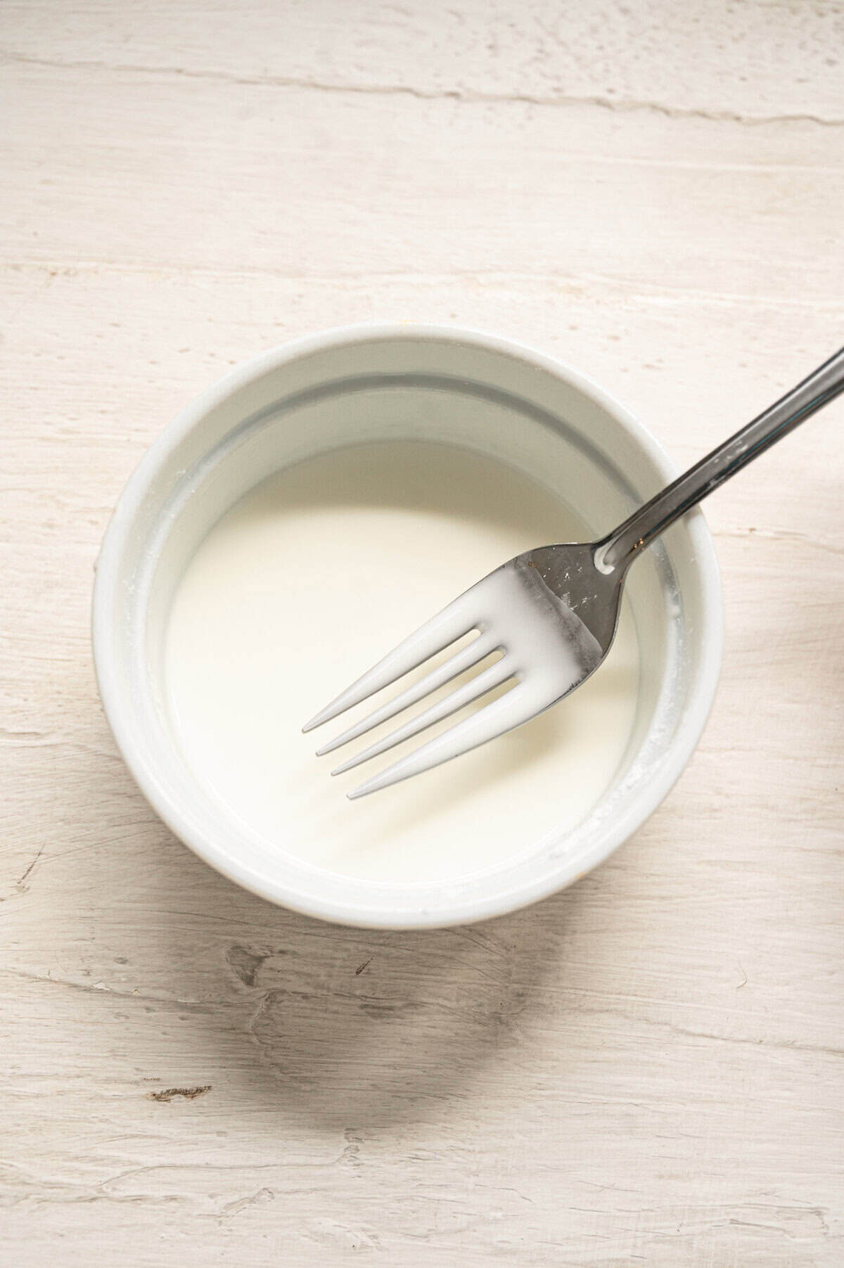 A fork being lifted out of a small bowl with cornstarch slurry to show what it should look like.