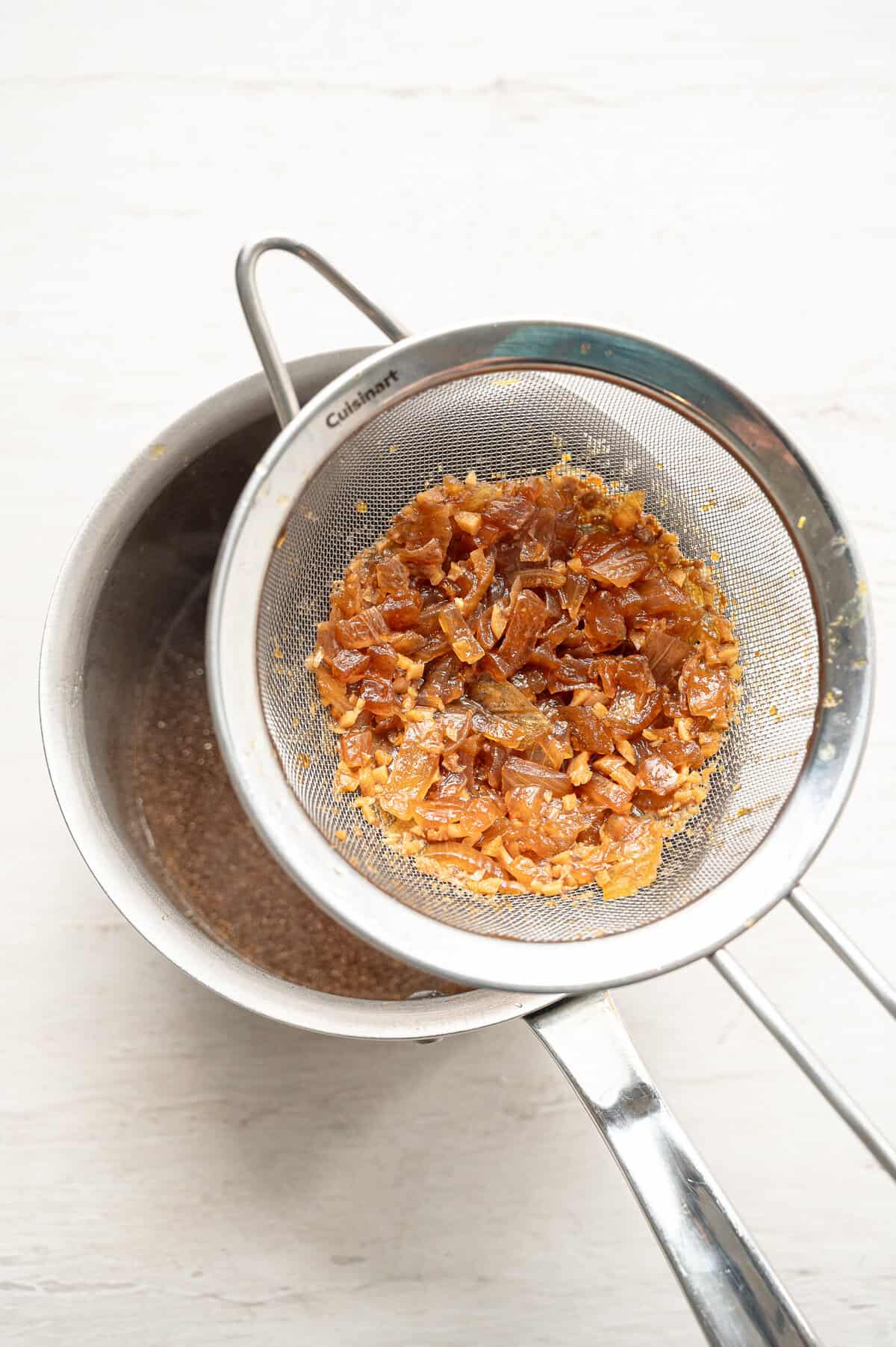 A metal colander straining chopped onions out of a teriyaki marinade to boil and make a sauce.