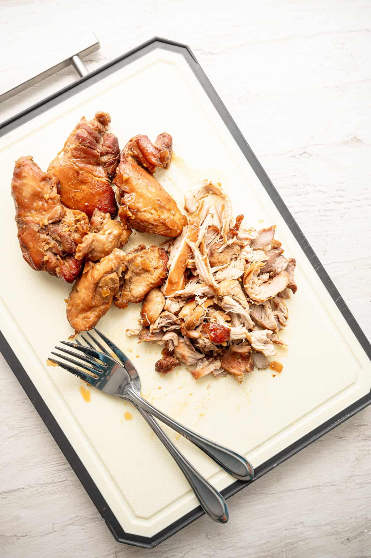 Boneless skinless chicken thighs that were cooked in teriyaki sauce being shredded on a cutting board.