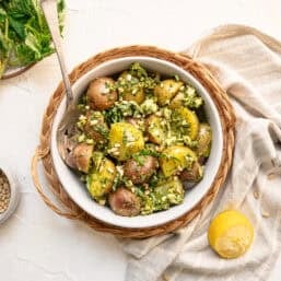 Pesto potato salad in a white bowl with a wicker basket around it.