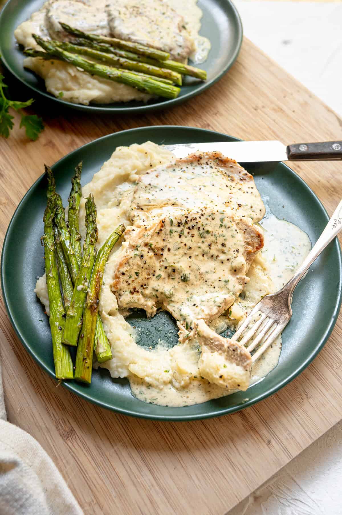 A fork with a piece of pork chop, mashed potatoes, and Boursin gravy being lifted from the plate.