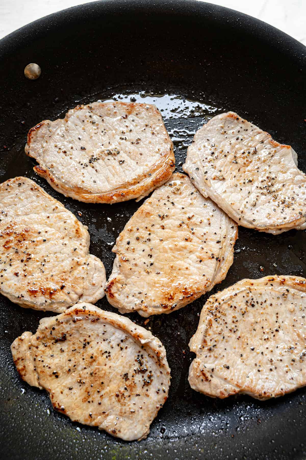 Boneless pork chops sauteing in a skillet.