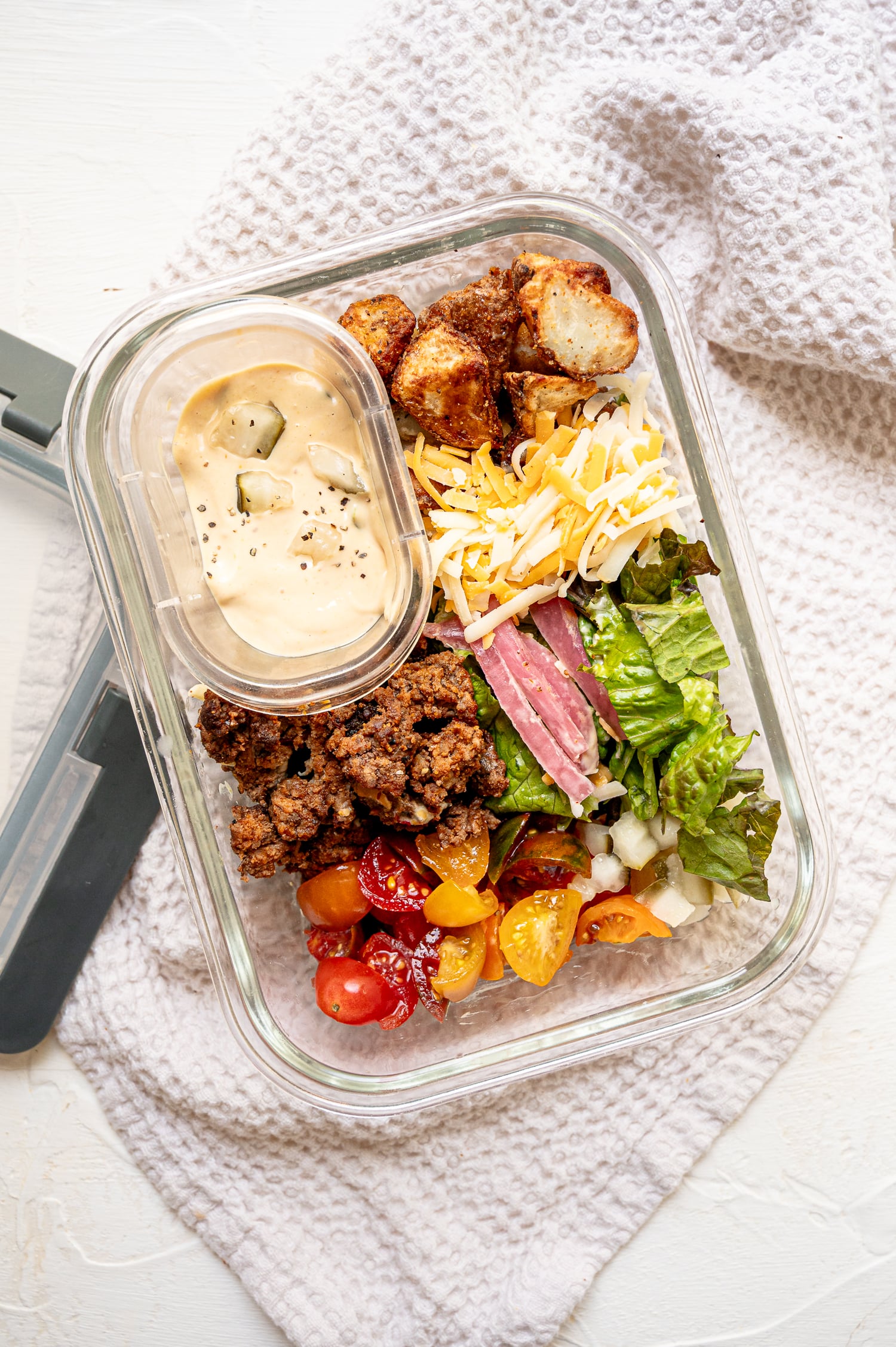 Ingredients for cheeseburger bowls in piles inside a glass container with the secret sauce kept separate.