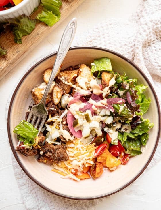 A cheeseburger bowl made up of roasted potato bites, crumbled ground beef, shredded cheese, lettuce, tomatoes, and pickled onions.