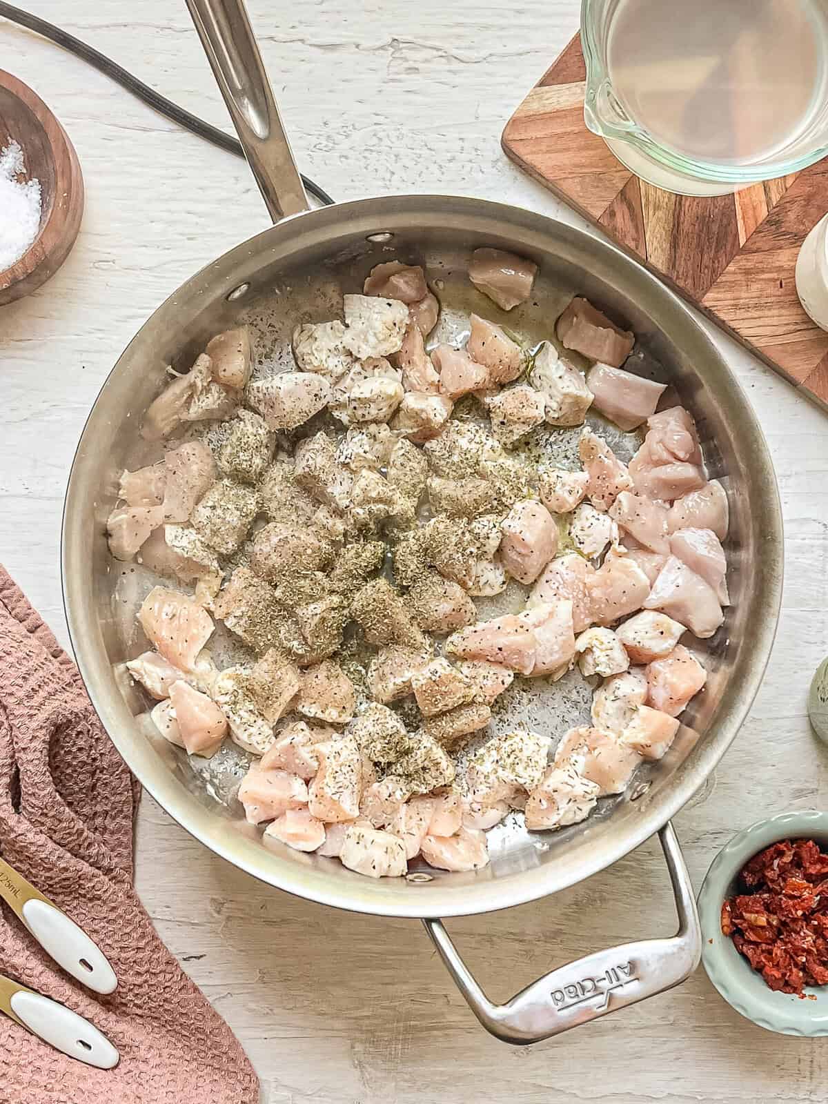 Raw chicken pieces sauteing in a skillet with Italian seasoning.