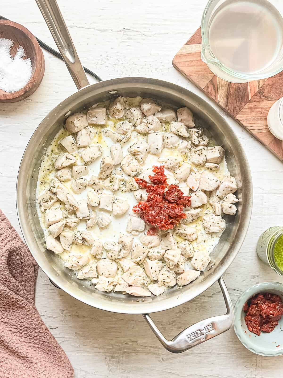 A skillet with cooked chicken chunks, sun-dried tomato pieces, and heavy cream.
