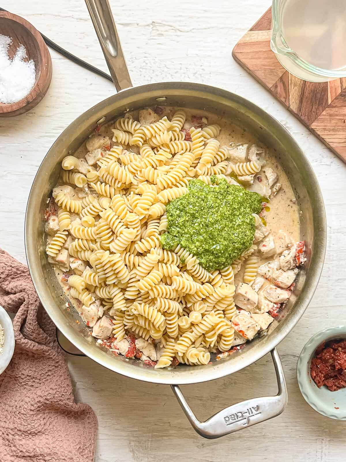 Ingredients for creamy pesto chicken pasta dumped in a skillet.