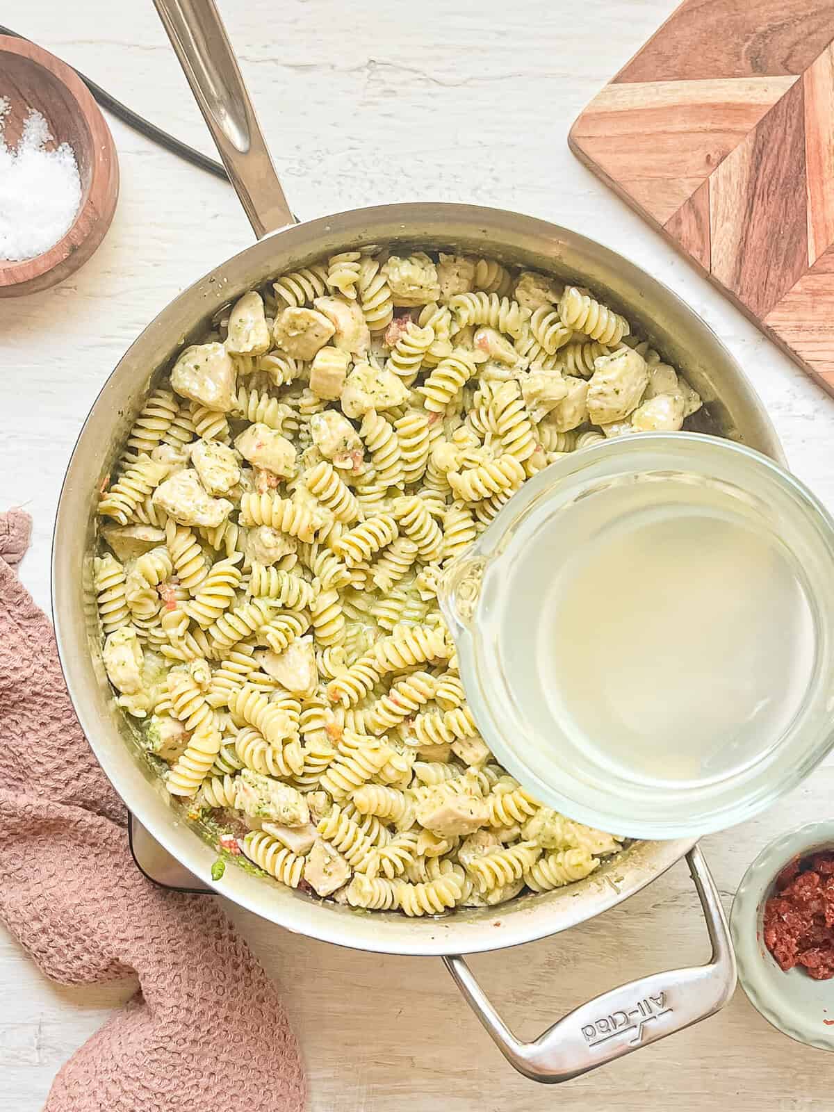 Pasta water being slowly added to a skillet with creamy chicken pesto pasta to thin it out a bit.