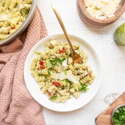 A skillet of creamy chicken pesto pasta next to a plate of it.
