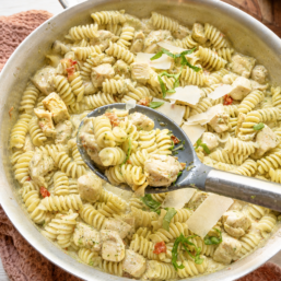 Creamy chicken pesto pasta being served from the skillet.