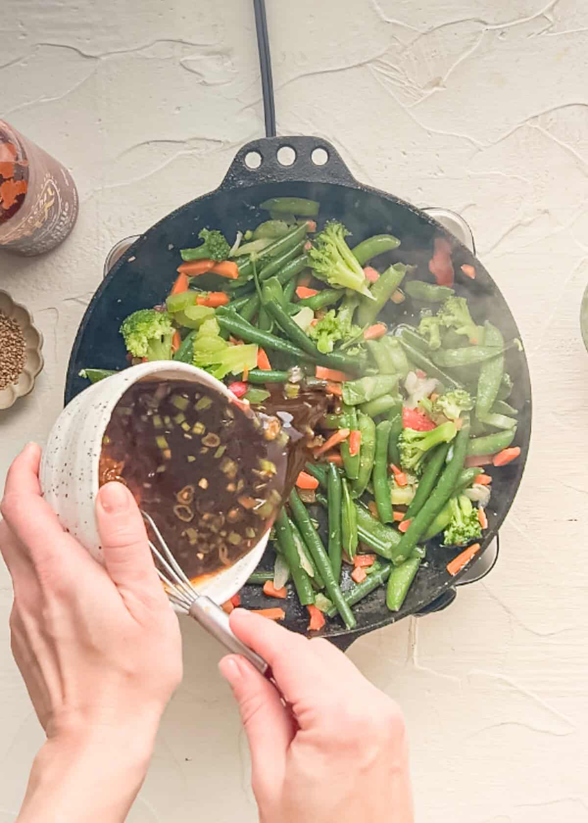 Steam coming off a skillet of stir-fry veggies as a homemade stir-fry sauce is being added.