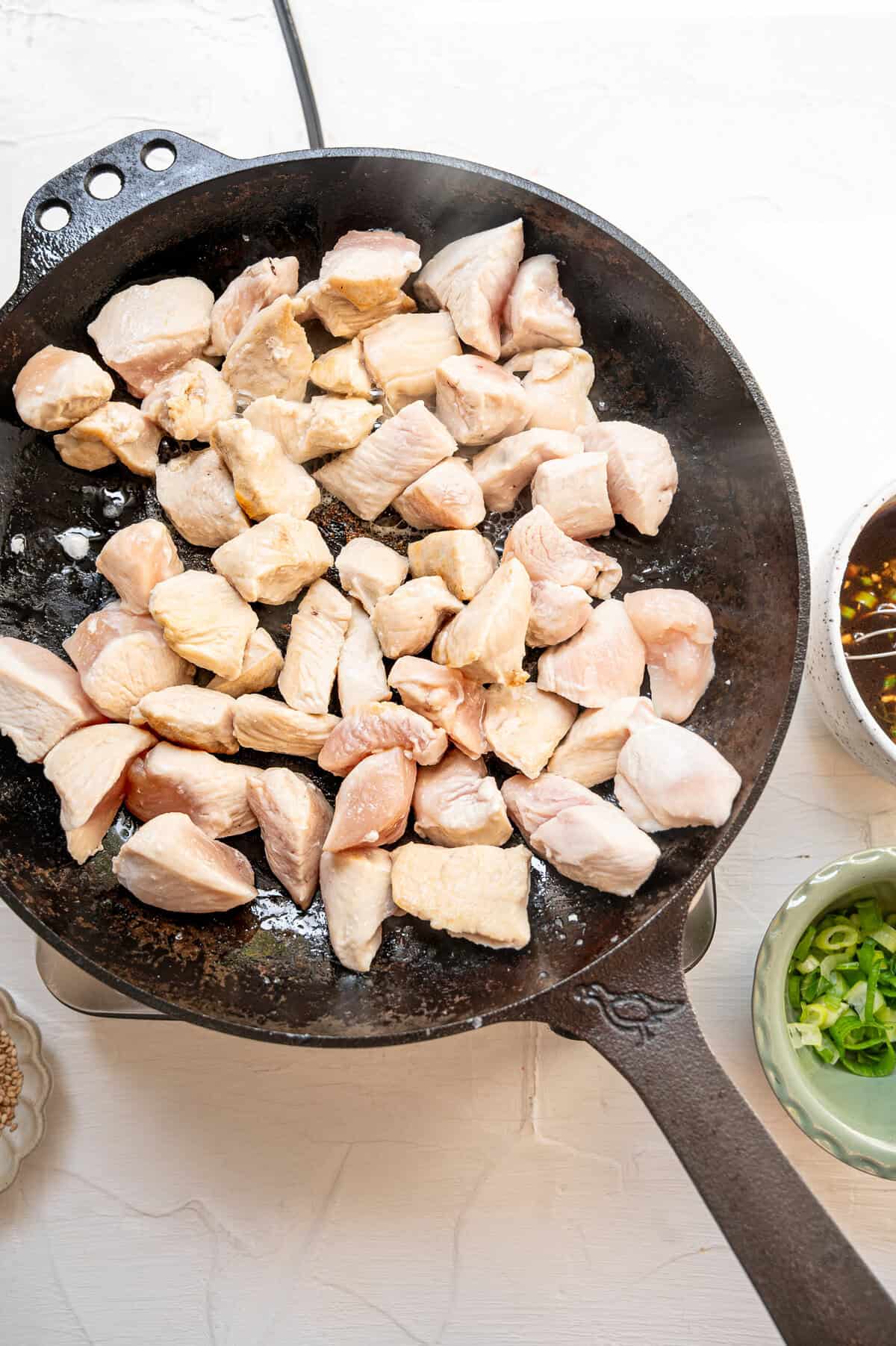 Chicken pieces being cooked in oil in a cast iron skillet.