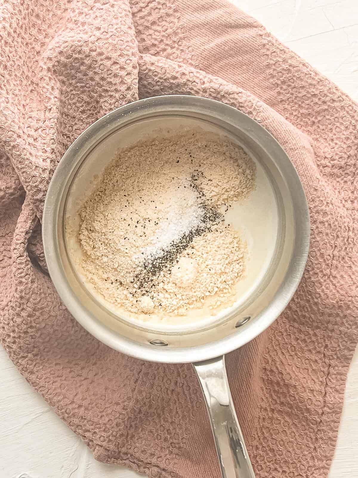 Grated Parmesan cheese being mixed into a cream sauce in a saucepan.