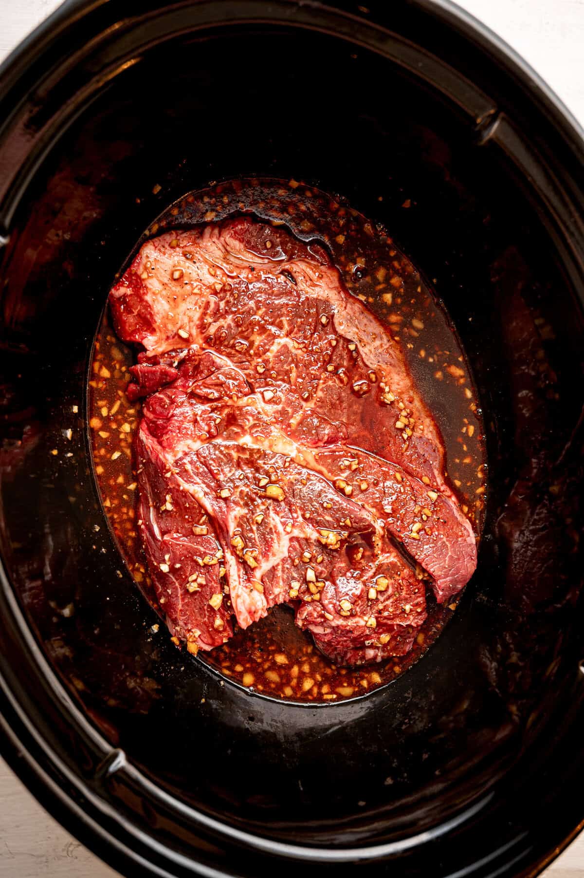 A roast in a slow cooker liner with Korean beef sauce poured over it before cooking.