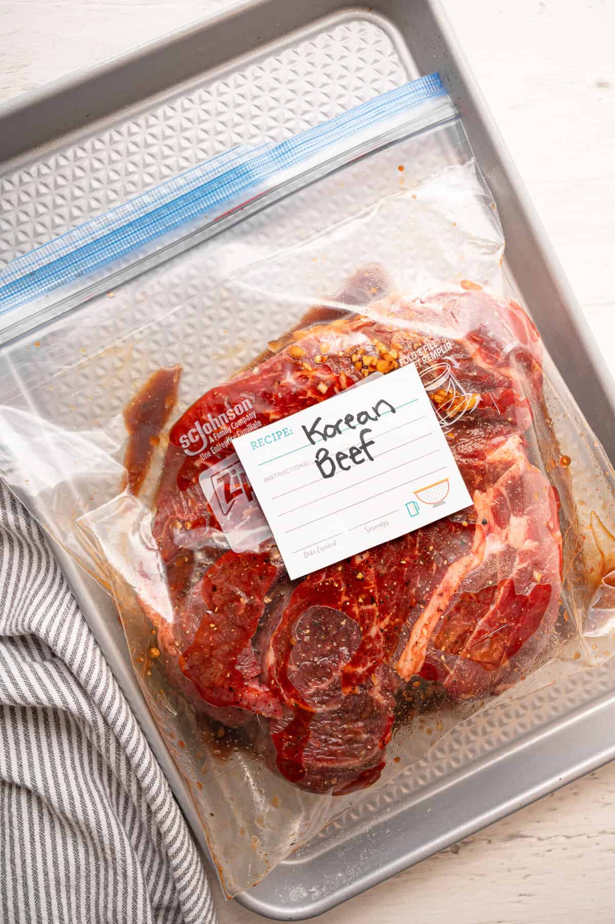 A freezer bag labeled Korean beef with a raw roast and sauce inside ready for the freezer.