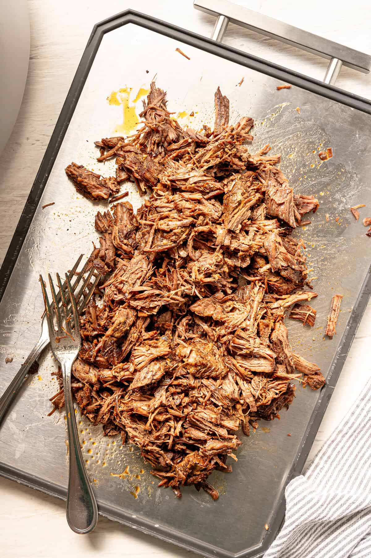 Two forks next to shredded Korean beef on a tray.