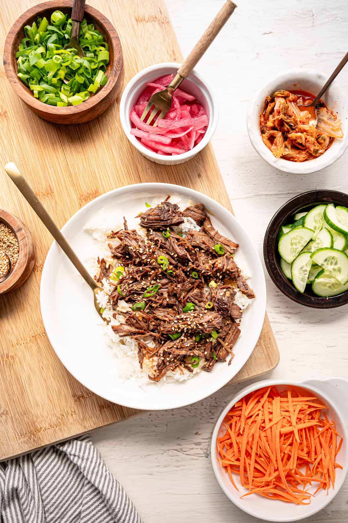 A plate with rice and shredded Korean beef with small bowls of toppings around it.